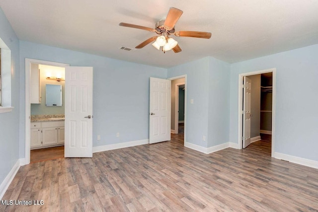 unfurnished bedroom featuring a closet, ensuite bathroom, a spacious closet, and light wood-type flooring