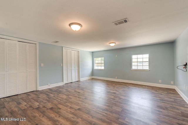 unfurnished bedroom featuring multiple closets, a textured ceiling, and dark hardwood / wood-style floors