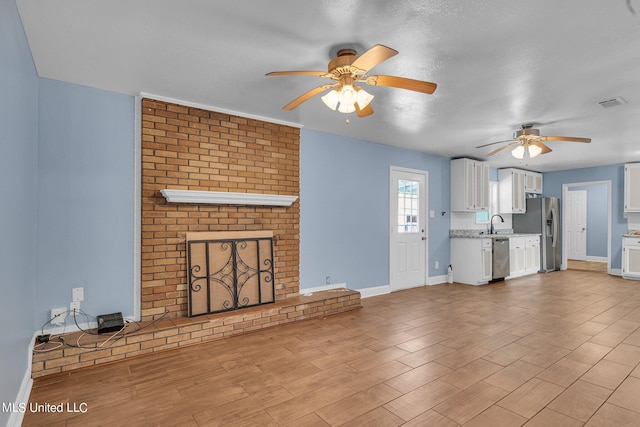 unfurnished living room with sink, a textured ceiling, a brick fireplace, ceiling fan, and light hardwood / wood-style flooring