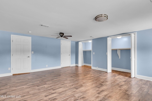 unfurnished bedroom featuring hardwood / wood-style flooring, two closets, and ceiling fan