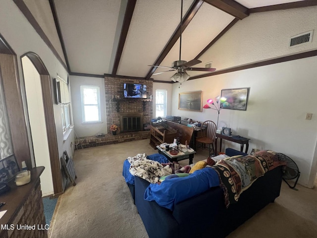 living room featuring vaulted ceiling with beams, ceiling fan, a brick fireplace, and carpet flooring