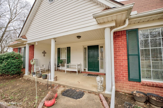 view of exterior entry with a porch and brick siding