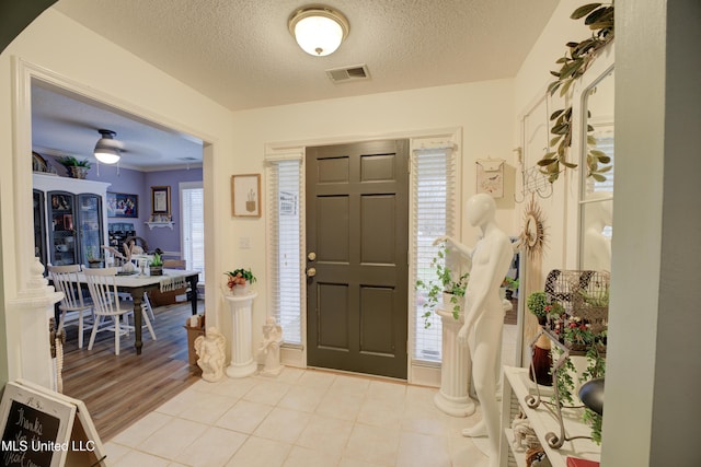 foyer entrance with visible vents, a textured ceiling, and tile patterned floors