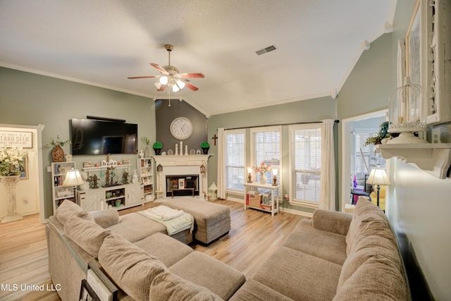 living area featuring lofted ceiling, ornamental molding, a glass covered fireplace, and visible vents