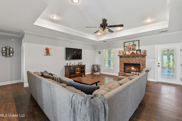 living room with a brick fireplace, dark wood-type flooring, crown molding, and a raised ceiling