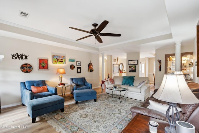 living room with ornate columns, ceiling fan, a raised ceiling, crown molding, and light hardwood / wood-style floors