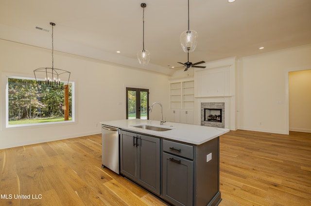 kitchen with pendant lighting, a center island with sink, sink, stainless steel dishwasher, and light hardwood / wood-style floors