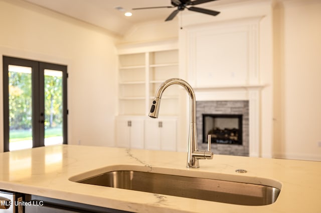 kitchen with light stone countertops, sink, ceiling fan, a stone fireplace, and vaulted ceiling