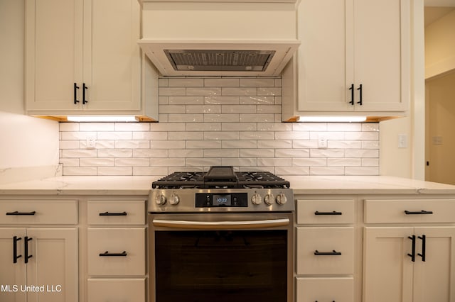 kitchen featuring decorative backsplash, white cabinets, light stone counters, and stainless steel range with gas stovetop