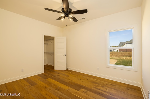 unfurnished bedroom with ceiling fan, a closet, a spacious closet, and dark hardwood / wood-style floors