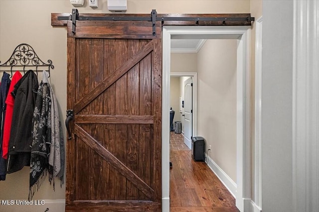 interior space featuring a barn door, wood finished floors, crown molding, and baseboards