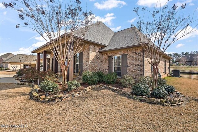 view of front facade with brick siding, a front lawn, fence, central AC, and roof with shingles