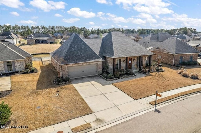 french country inspired facade featuring brick siding, a residential view, concrete driveway, roof with shingles, and a garage