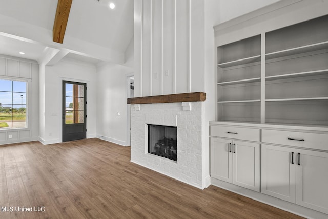 unfurnished living room with built in features, beamed ceiling, light wood-type flooring, and a fireplace