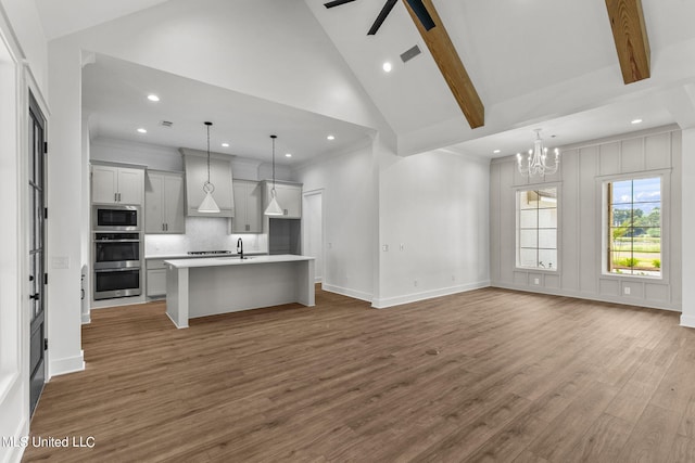 kitchen with wood-type flooring, appliances with stainless steel finishes, decorative light fixtures, decorative backsplash, and a center island with sink