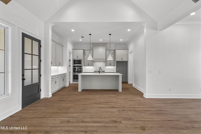 kitchen with appliances with stainless steel finishes, dark hardwood / wood-style flooring, pendant lighting, and an island with sink