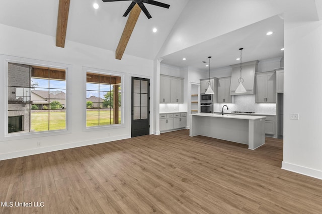 kitchen with hardwood / wood-style flooring, an island with sink, custom range hood, sink, and decorative light fixtures