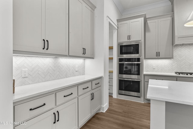 kitchen with appliances with stainless steel finishes, crown molding, dark wood-type flooring, and backsplash