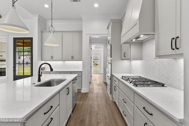 kitchen featuring sink, pendant lighting, custom exhaust hood, appliances with stainless steel finishes, and light stone counters