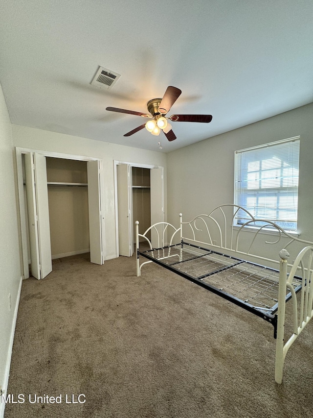 unfurnished bedroom featuring baseboards, visible vents, ceiling fan, carpet flooring, and two closets