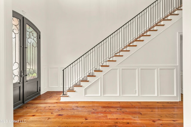 entrance foyer with a decorative wall, french doors, stairway, and wood finished floors