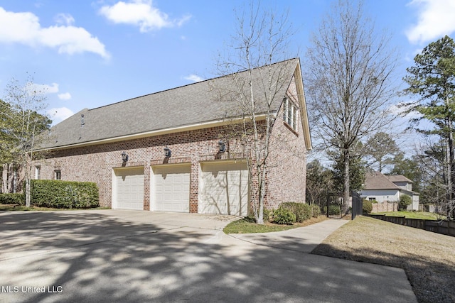 view of property exterior featuring brick siding, roof with shingles, driveway, and fence