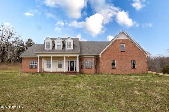 view of front facade with a porch, roof with shingles, a front yard, and brick siding