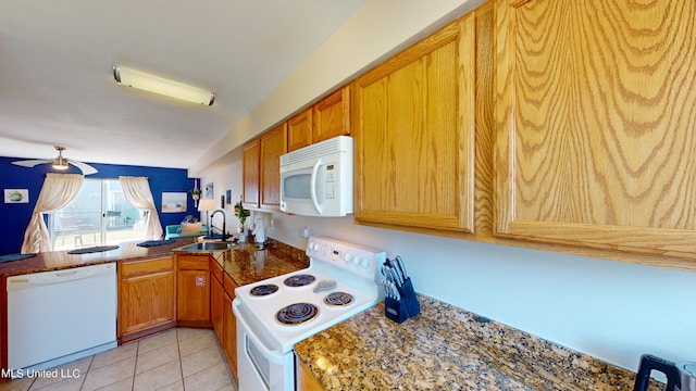 kitchen with dark stone counters, sink, light tile patterned floors, white appliances, and ceiling fan