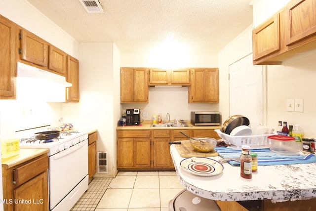 kitchen featuring sink, white gas stove, a textured ceiling, and light tile patterned flooring