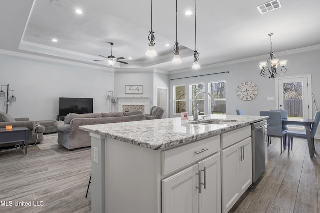 kitchen with a sink, a tray ceiling, light wood-style floors, and dishwasher