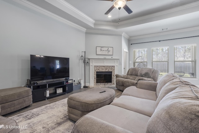 living area featuring a high end fireplace, visible vents, ornamental molding, wood finished floors, and a raised ceiling