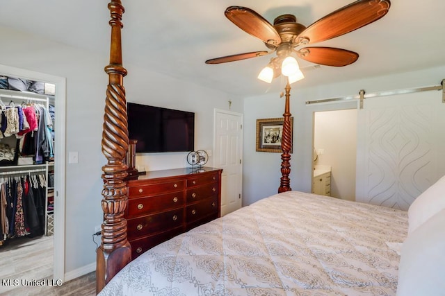 bedroom featuring a barn door, a walk in closet, a closet, wood finished floors, and ceiling fan