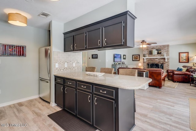 kitchen with freestanding refrigerator, a peninsula, ceiling fan, light wood-type flooring, and a fireplace