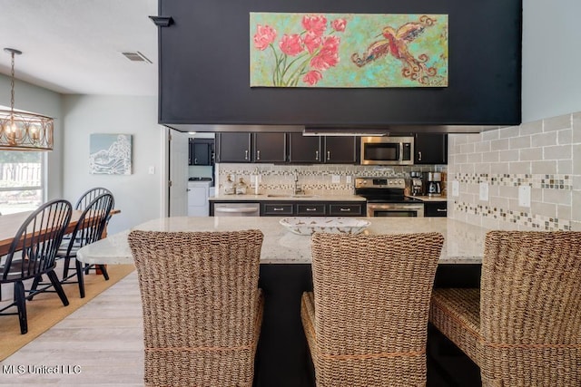 kitchen featuring appliances with stainless steel finishes, backsplash, a kitchen breakfast bar, a sink, and light stone countertops