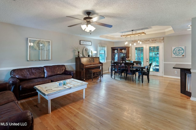 living area featuring baseboards, a textured ceiling, a raised ceiling, a ceiling fan, and light wood-style flooring