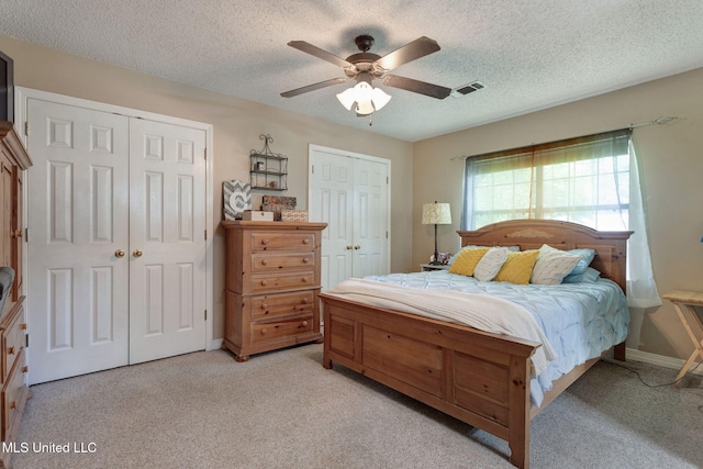 bedroom featuring ceiling fan, a textured ceiling, visible vents, two closets, and light carpet