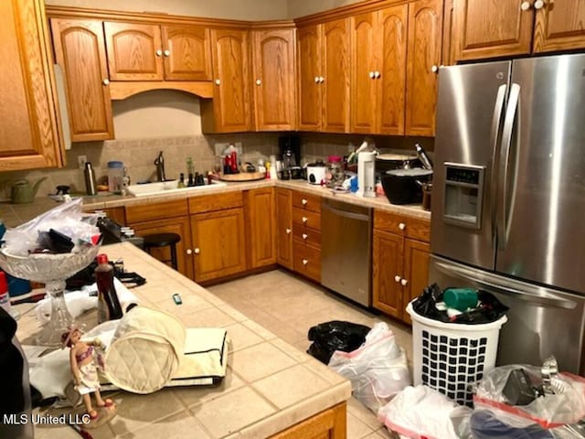 kitchen with brown cabinetry, tile countertops, appliances with stainless steel finishes, a sink, and backsplash