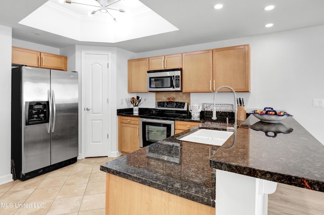 kitchen with light brown cabinets, a sink, a tray ceiling, a peninsula, and appliances with stainless steel finishes