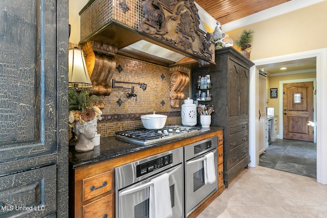 kitchen featuring stainless steel appliances, dark stone counters, decorative backsplash, light tile patterned flooring, and ornamental molding