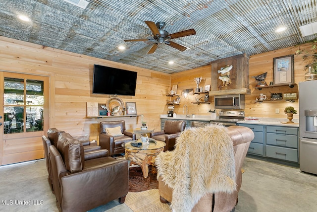 living room featuring ceiling fan, wooden walls, and sink