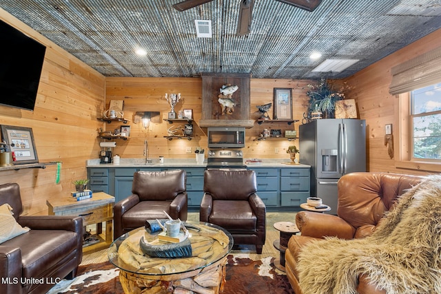 living room with wood walls, sink, ceiling fan, and light carpet