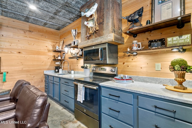 kitchen with wood walls, sink, blue cabinetry, light stone counters, and stainless steel appliances