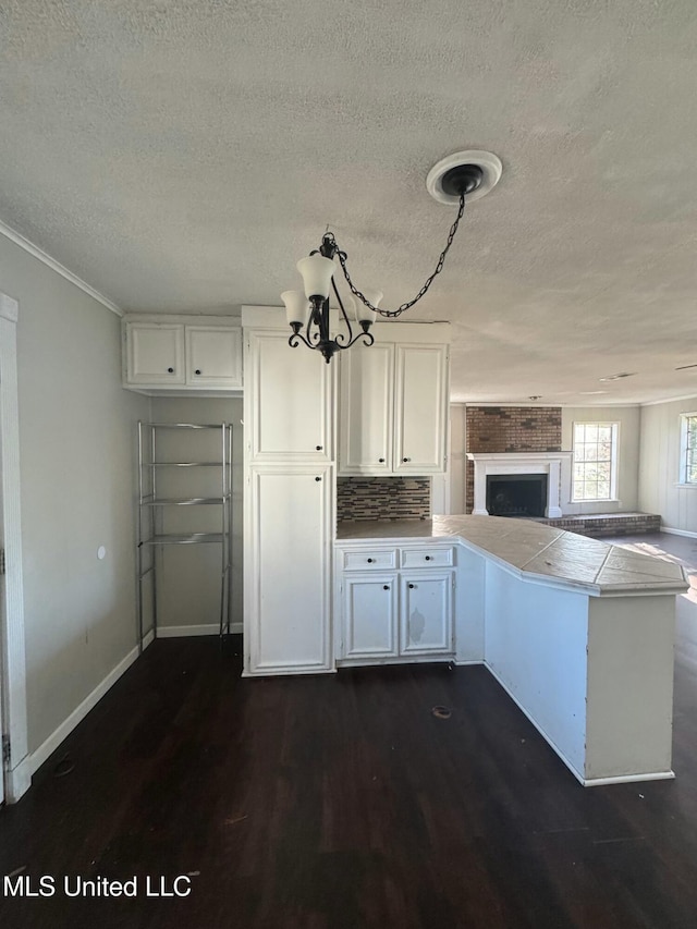 kitchen with baseboards, a peninsula, dark wood-type flooring, white cabinetry, and open floor plan