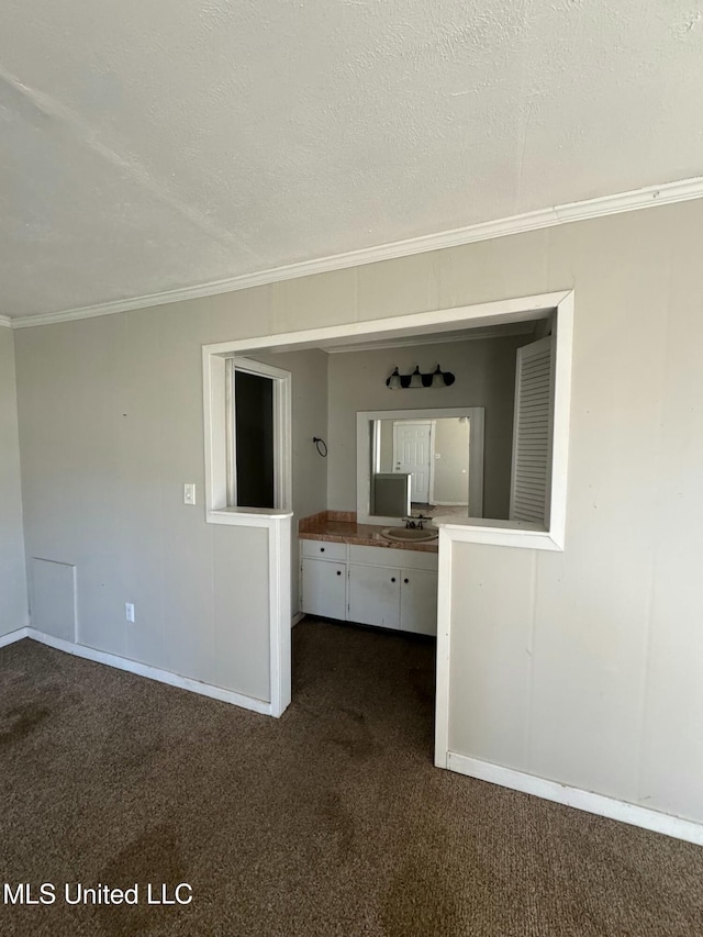 unfurnished room with a sink, a textured ceiling, crown molding, dark colored carpet, and baseboards