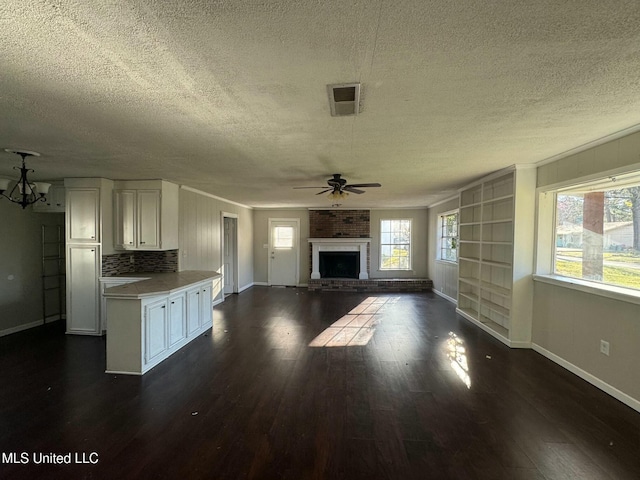 unfurnished living room with a wealth of natural light, dark wood-style floors, a fireplace, and visible vents