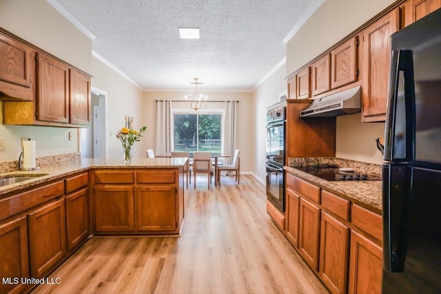 kitchen featuring under cabinet range hood, brown cabinets, a peninsula, an inviting chandelier, and black appliances