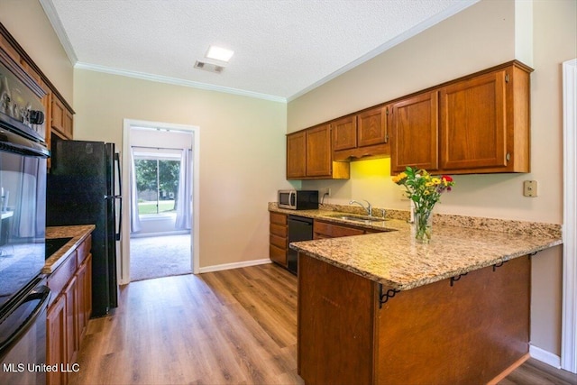 kitchen with visible vents, black appliances, a sink, a peninsula, and brown cabinetry