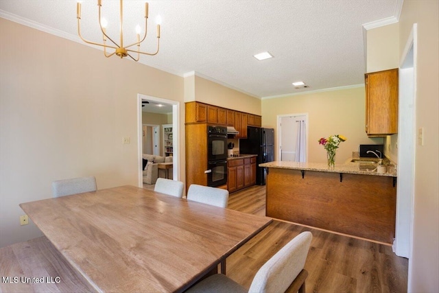 dining area featuring a notable chandelier, light wood-style flooring, crown molding, and a textured ceiling