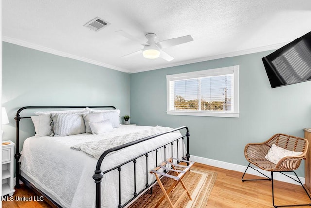 bedroom featuring baseboards, visible vents, wood finished floors, a textured ceiling, and crown molding