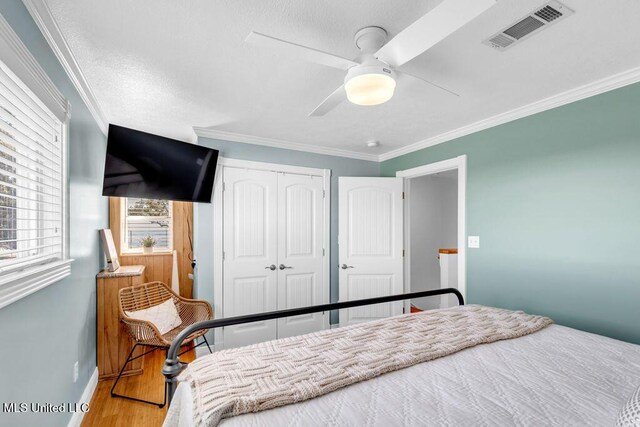 bedroom featuring a closet, wood finished floors, visible vents, and crown molding